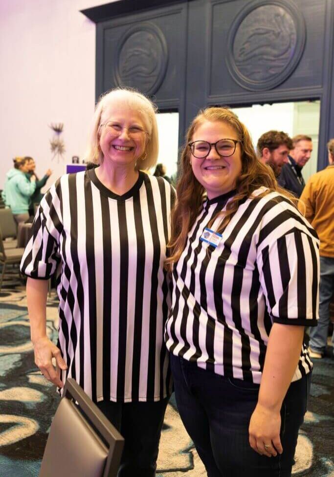 Two women in Referee jerseys pose in conference room.